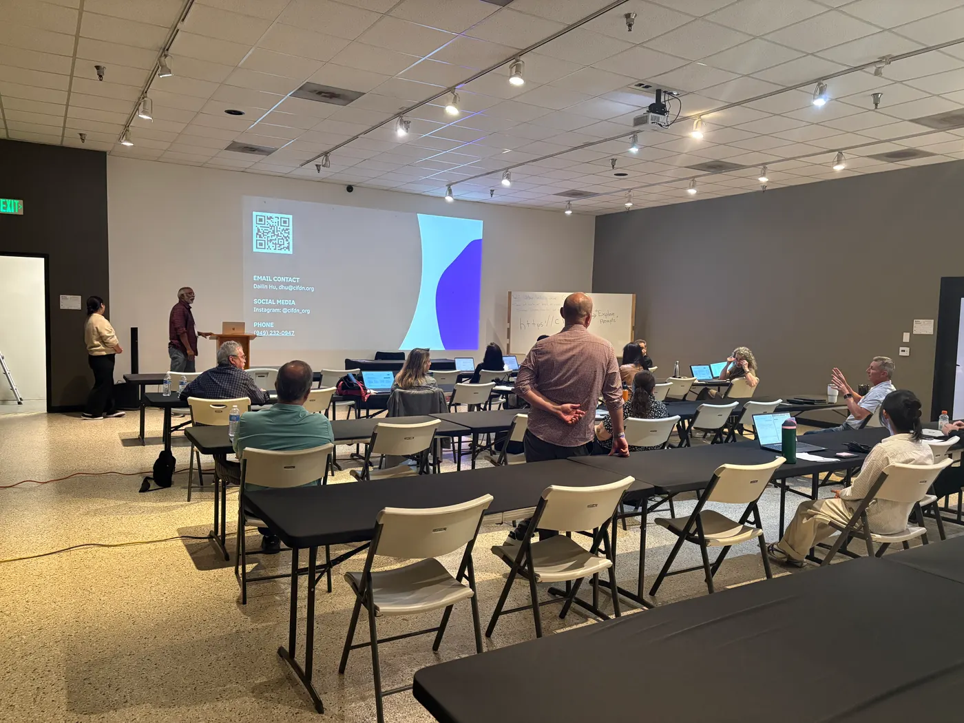 Small business owners seated at tables with open laptops while a participant stands to ask a question.